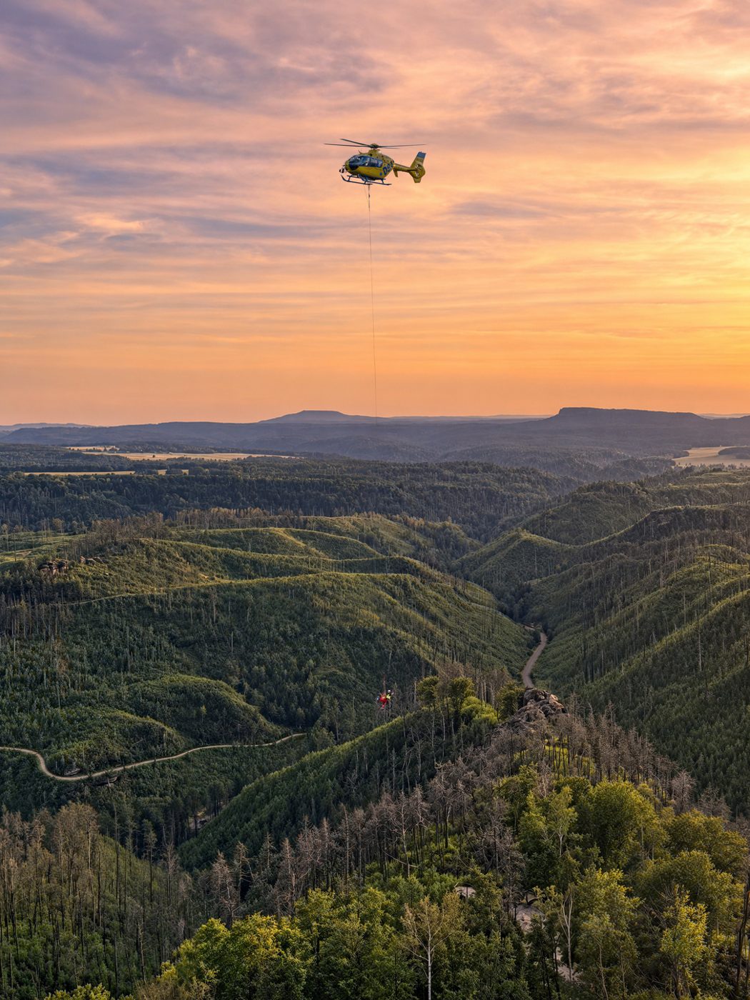 Rescue helicopter over a forested landscape at sunset